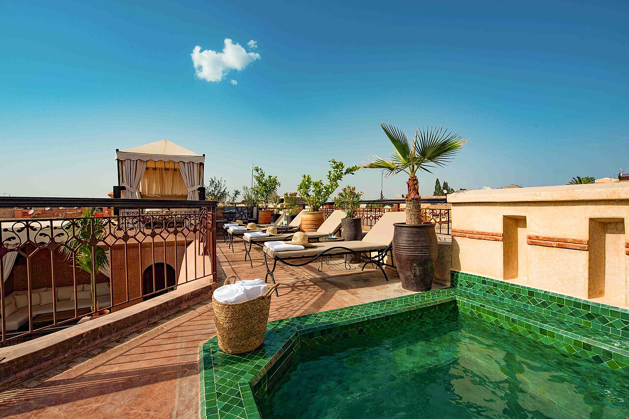 Terrace of a medina riad with a green zellige-tiled pool and sun loungers
