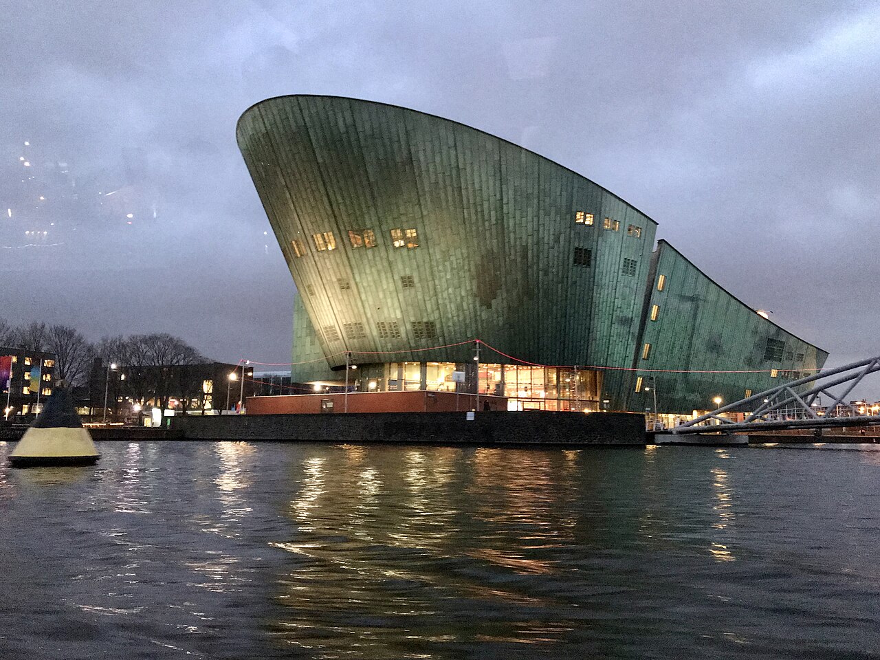 The green NEMO Science Museum building at dusk, on the Oosterdok