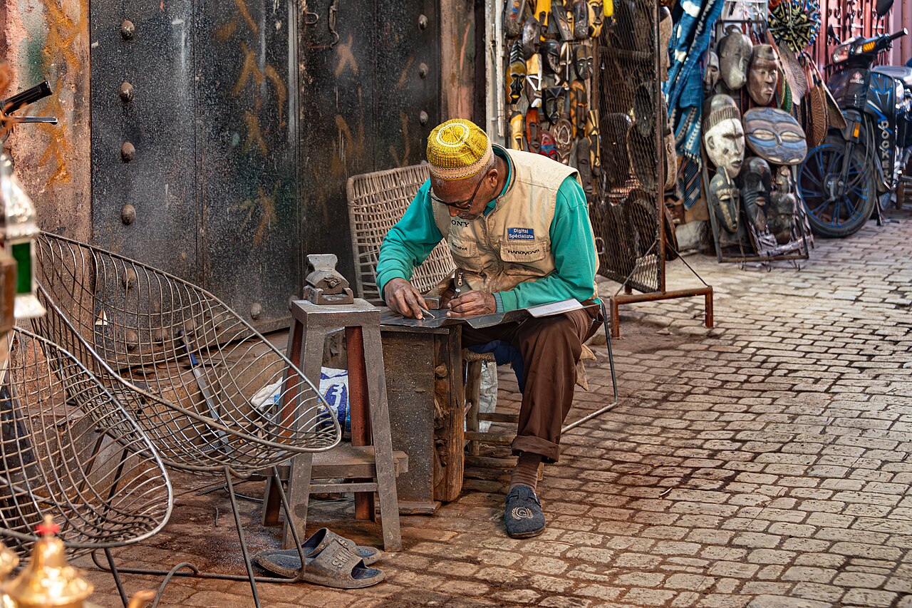 Artisan ciselant une plaque de métal devant son atelier, dans une ruelle de la médina de Marrakech
