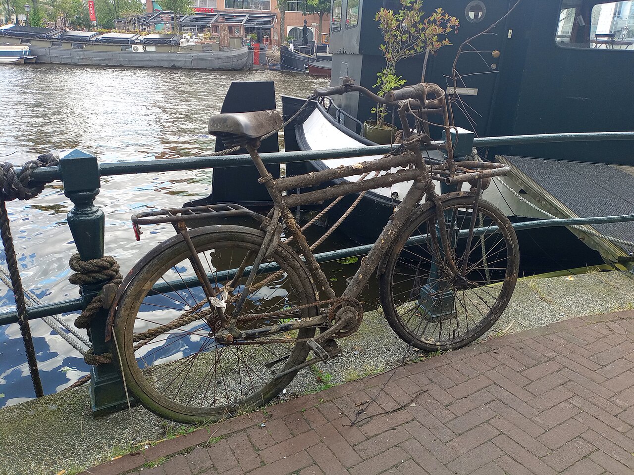 Een oude, verroeste fiets die uit een gracht is gevist, tegen een reling