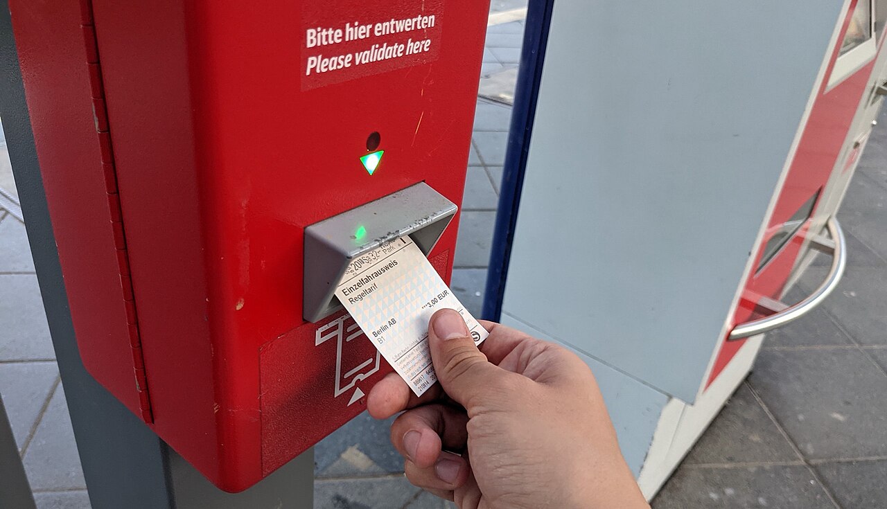 Validation d'un billet papier dans un composteur rouge du réseau VBB