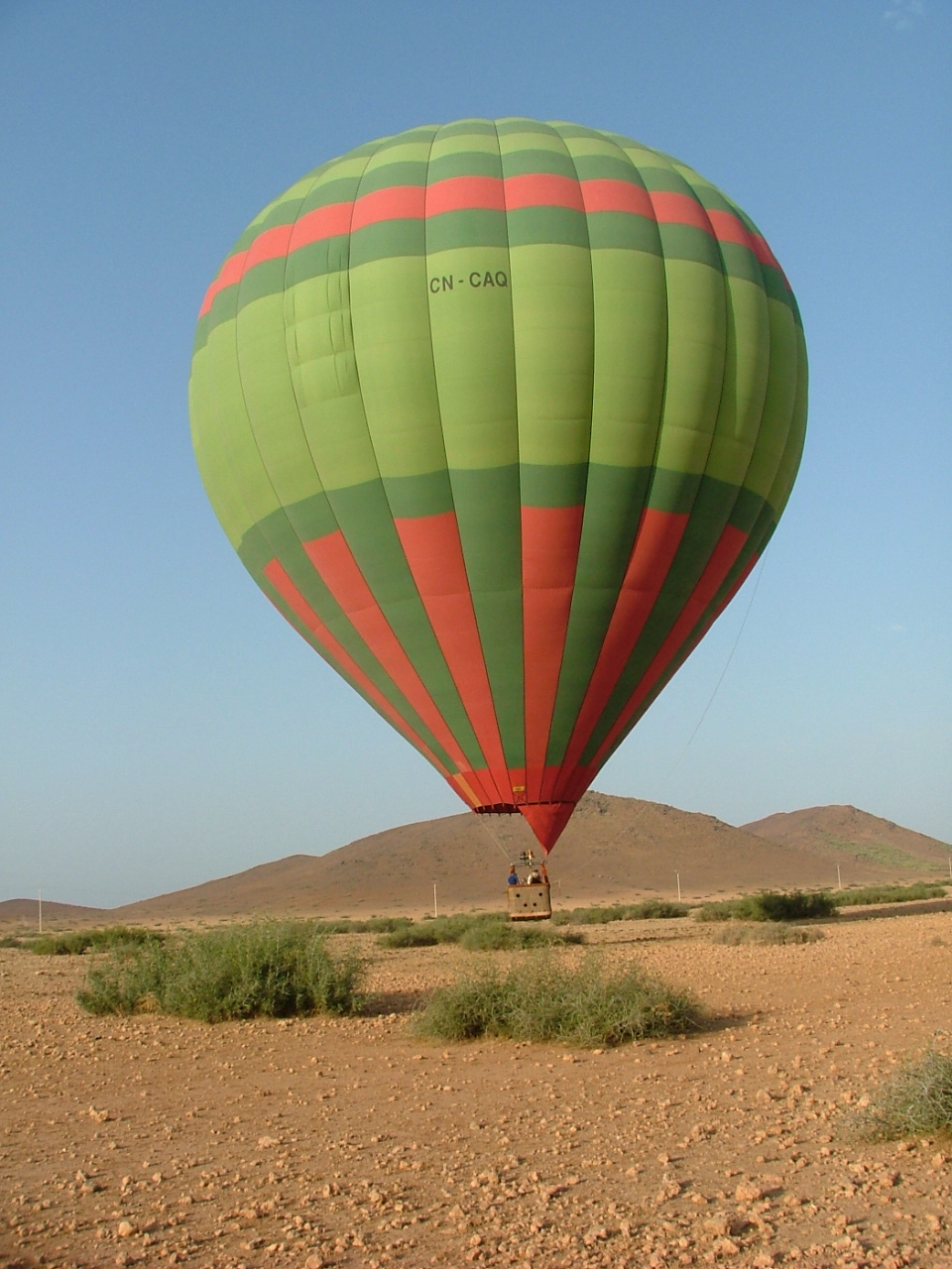 Une montgolfière posée sur la terre ocre devant les collines au nord de Marrakech