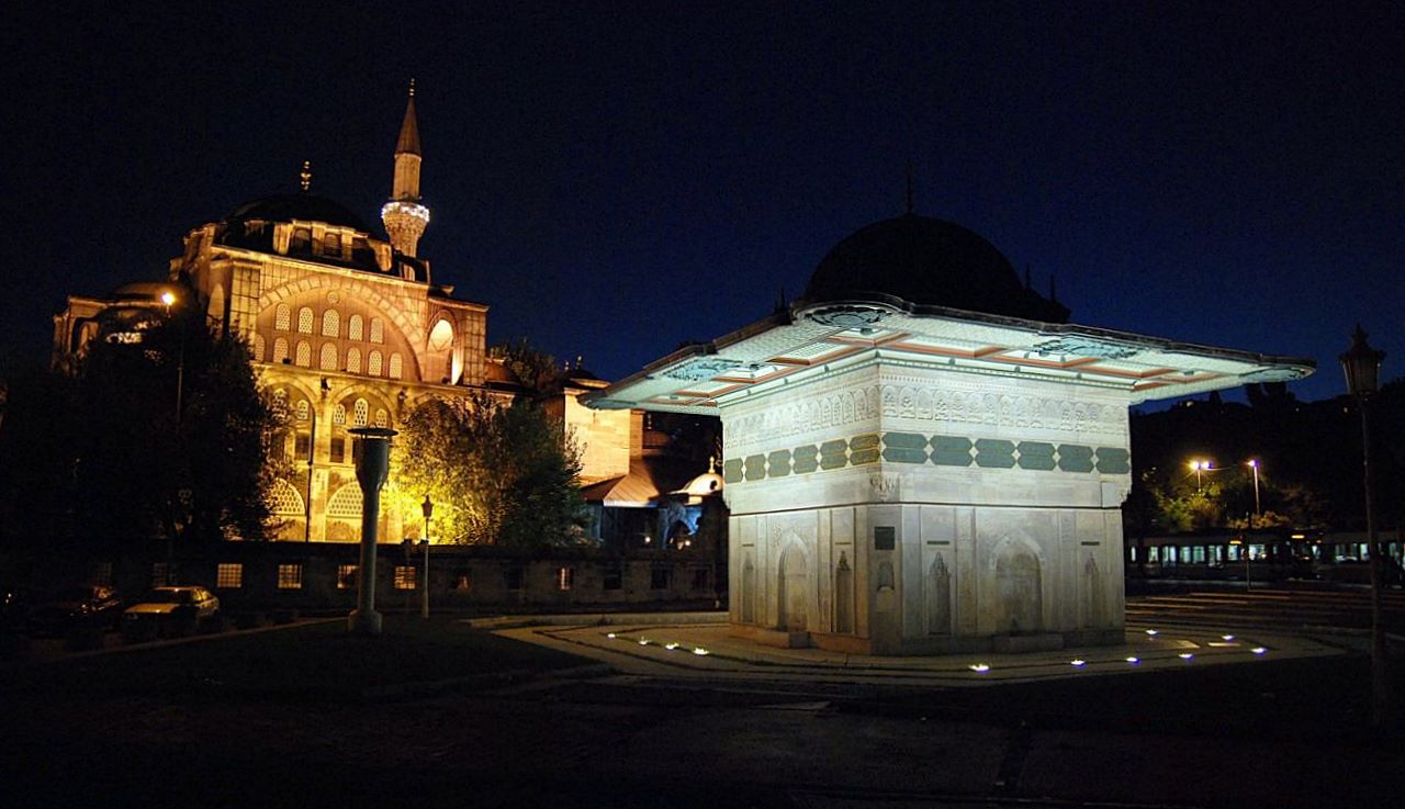 La mosquée Kılıç Ali Paşa illuminée la nuit, derrière la fontaine de Tophane