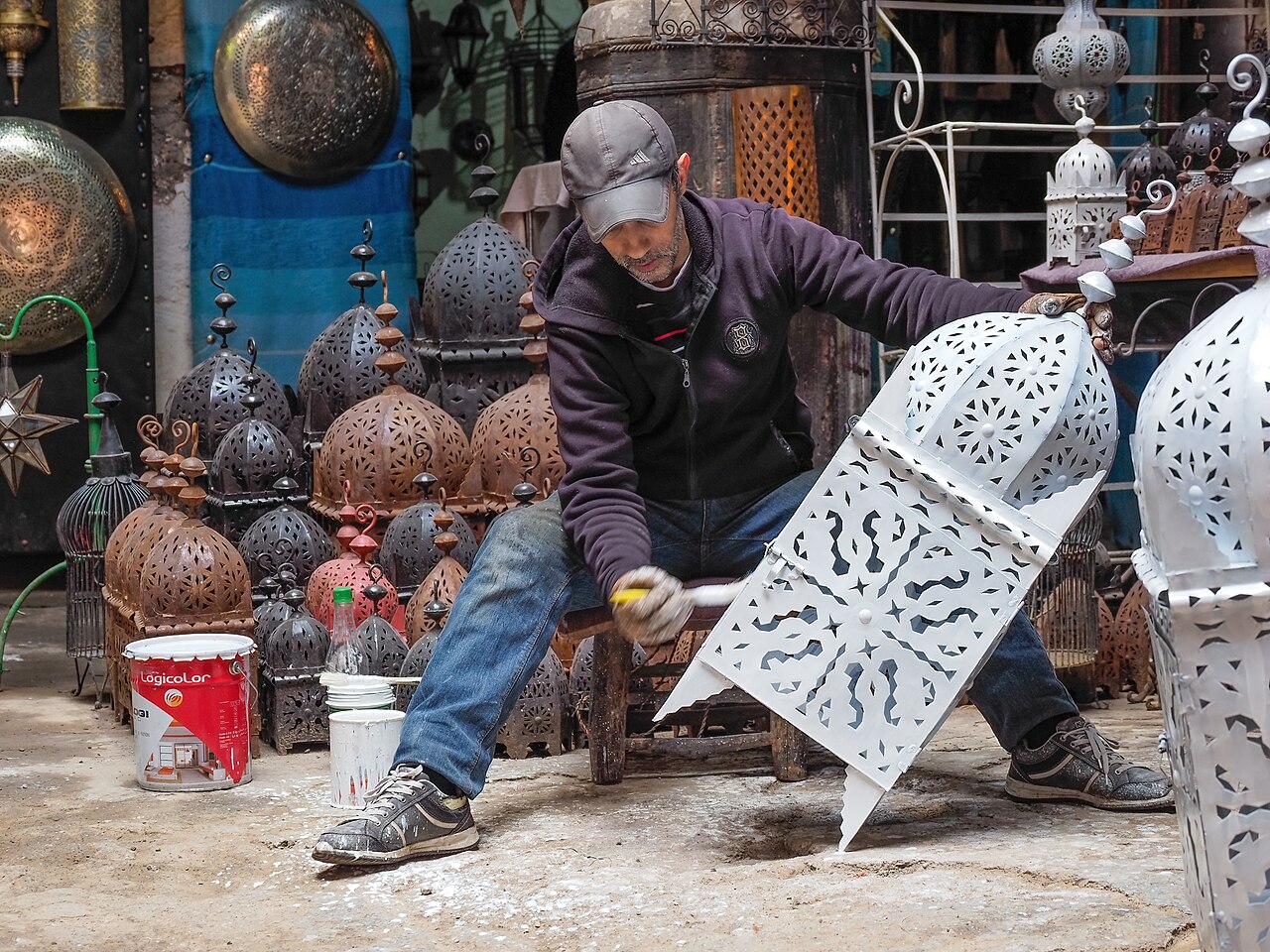 Artisan peignant une grande lanterne en métal ajouré dans un atelier de la médina de Marrakech