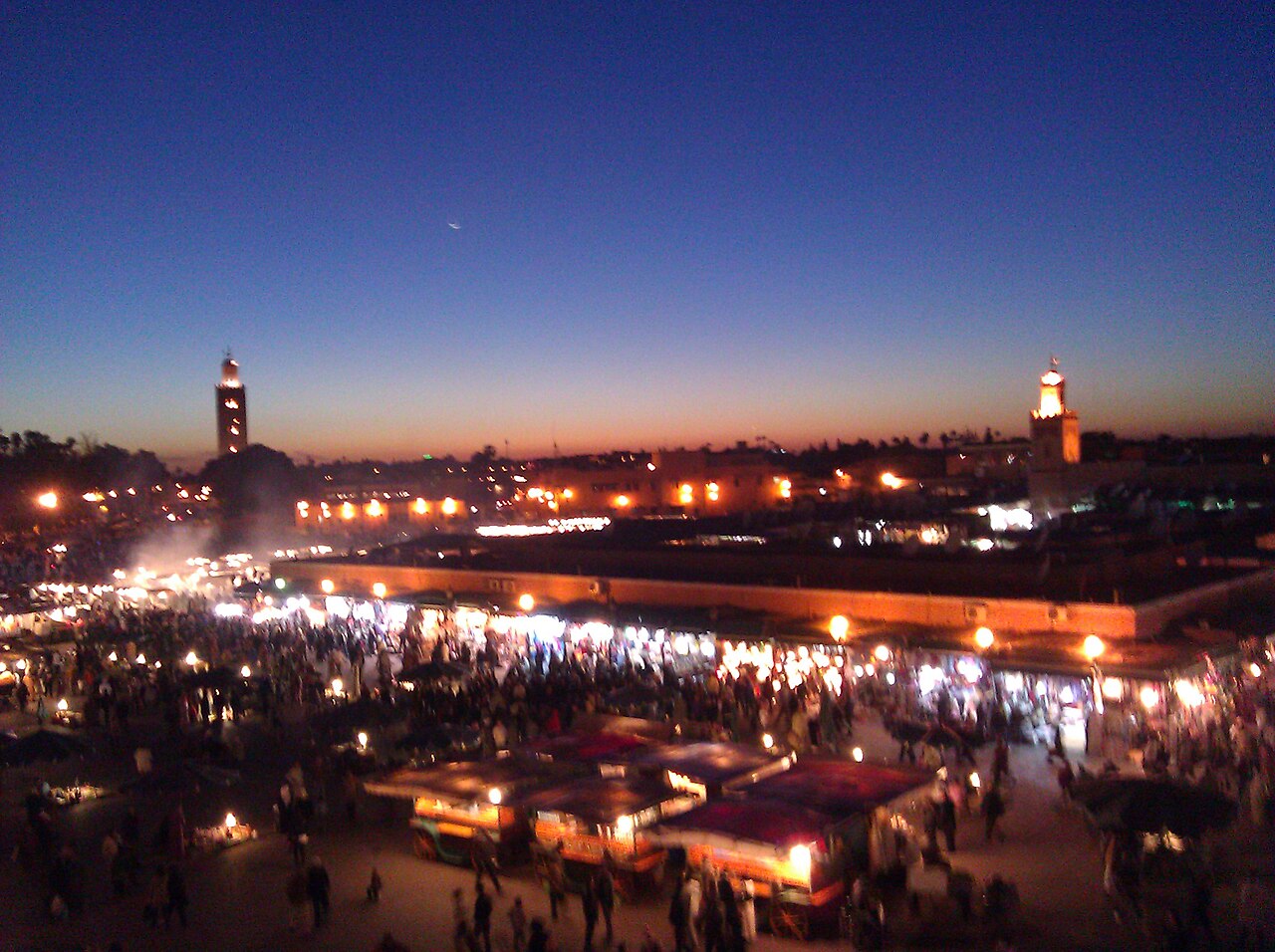 Jemaa el-Fna square lit up at nightfall, with the Koutoubia minaret